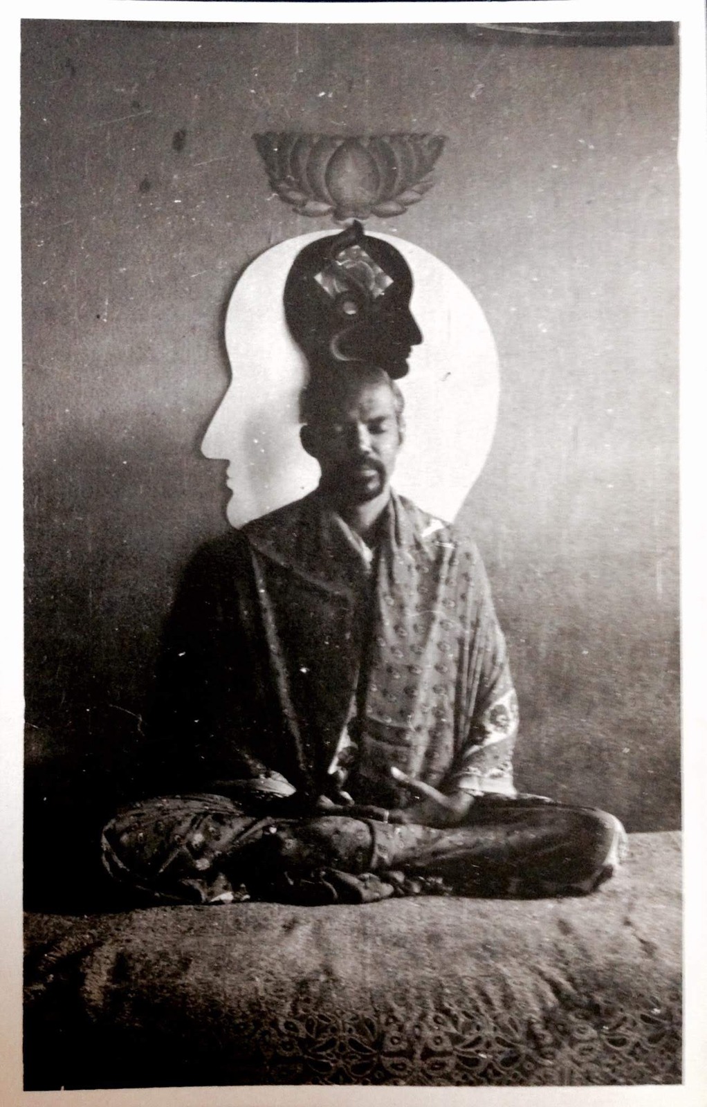 J Srividya seated in meditation with a painting of bodiless heads behind him